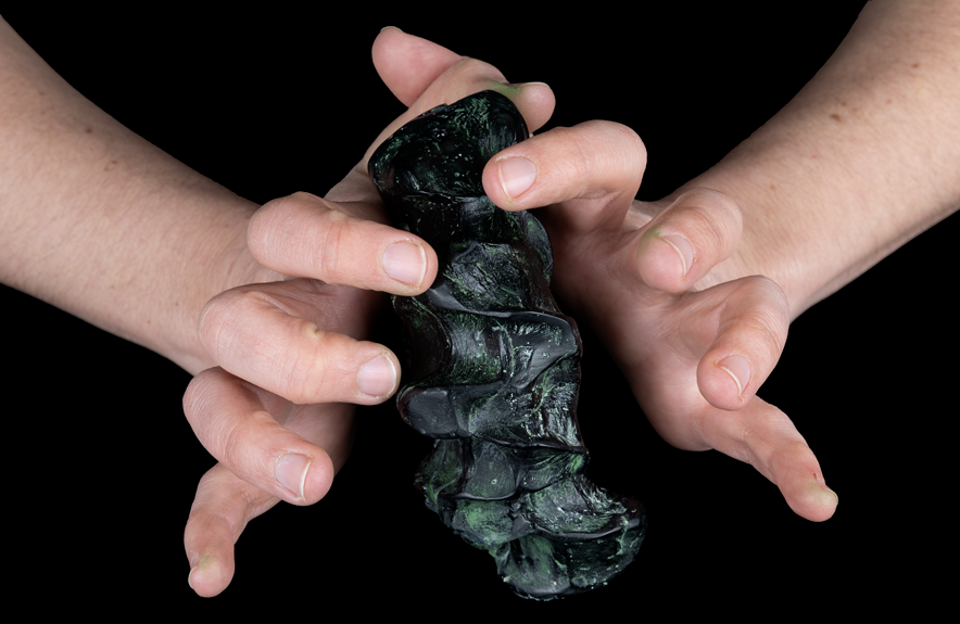 Entre deux mains, un objet noirâtre qui semble conserver la marque des doigts qui le tiennent.