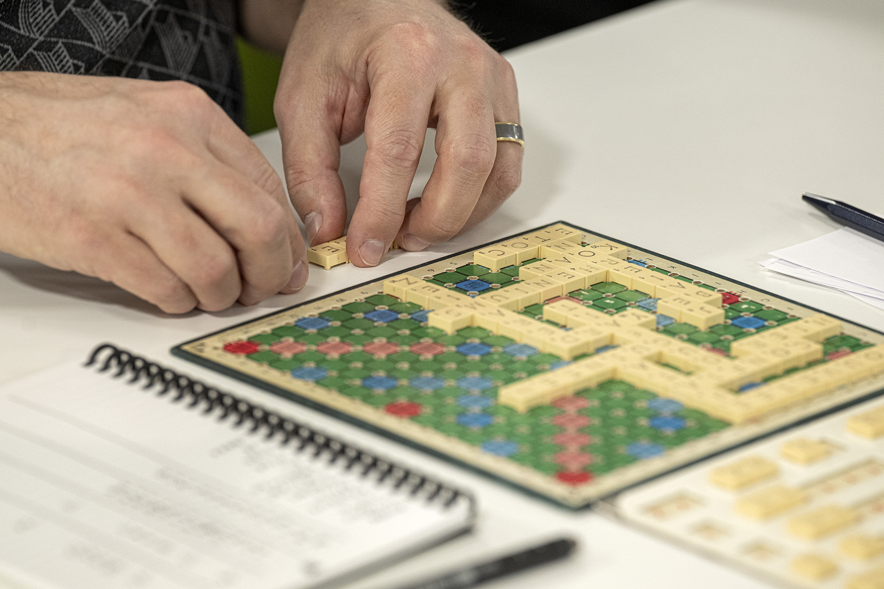 Gros plan sur un plateau de Scrabble où l'on peut voir les mains du joueur en train de former un mot