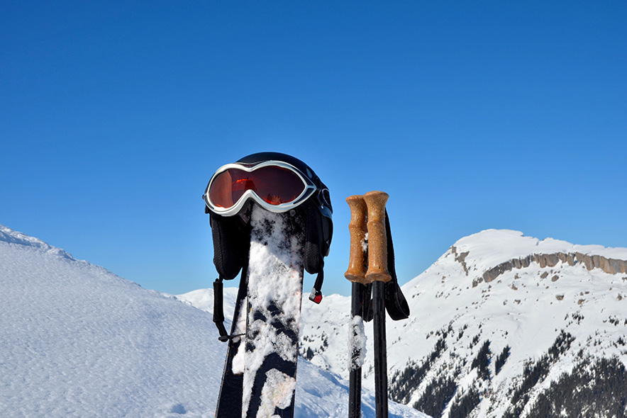 Un casque de ski posé sur des skis et des bâtons de ski plantés dans la neige.