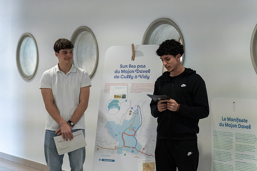 deux jeunes gymnasiens devant un panneau de l'exposition où on lit "Sur les pas du major Davel, de Cully à Vidy".