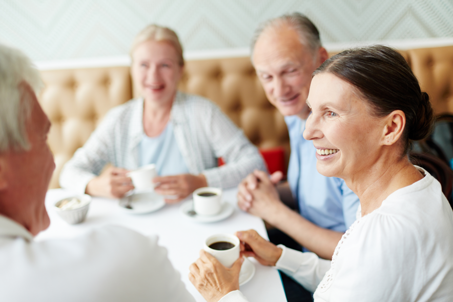 Trois personnes seniors prennent le café autour d'une table en bavardant.