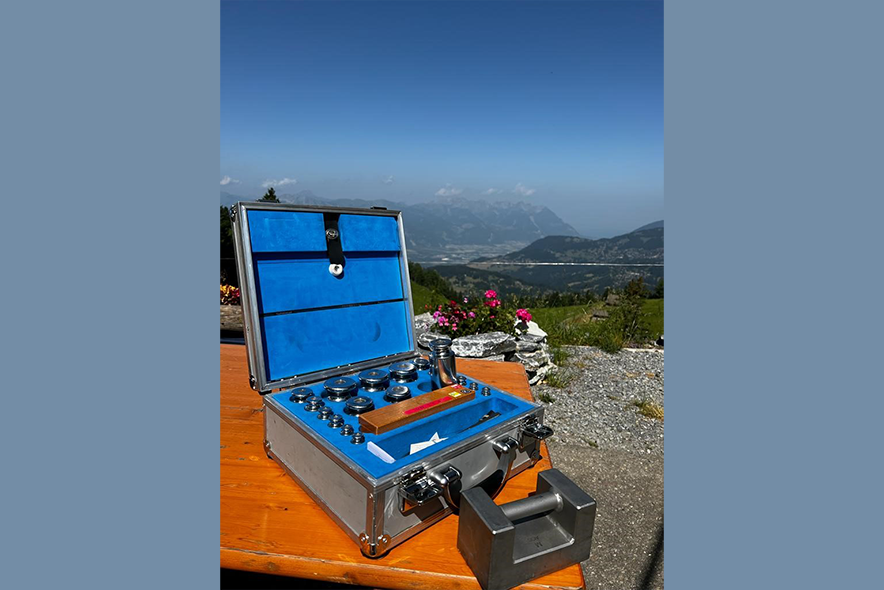 Valise des étalons poids posée sur une table, en haut d'un alpage avec la vue sur Aigle et le Léman en fond.