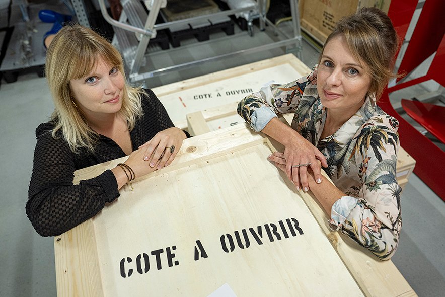 Les deux personnes posent, dans les réserves du musée, accoudées à une caisse de transport d'oeuvres sur laquelle on lit: "Côté à ouvrir"