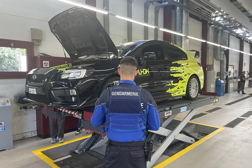 Photographie: Policier devant une voiture au SAN avec capot ouvert, se faisant inspecter.