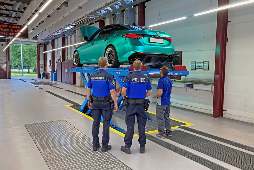 Illustration: Policier, gendarme et expert du SAN inspectant une voiture modifiée, sur un monte charge.