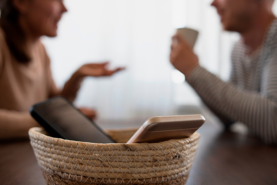 Un couple face à face dialogue. Ils sont dans le flou. Au premier plan, une corbeille contient deux mobiles.