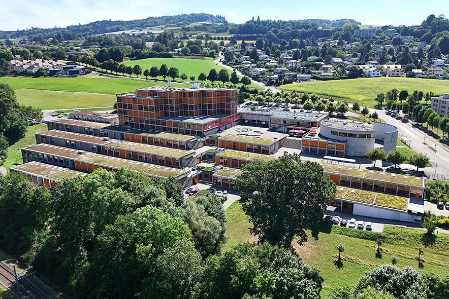 Vue aérienne des bâtiments. Au premier plan, en bas, un rideau d'arbres.