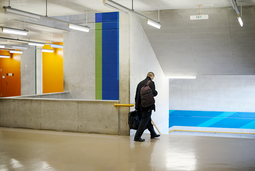 Un homme s'apprête à descendre un escalier. On voit de grands aplats de pleinture bleue et verte dans la cage d'escalier.
