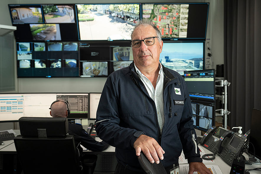 Monsieur Merminod est dans une salle de sécurité. Derrière lui, un mur d'écrans de surveillance. Un collaborateur est de dos, un casque audio sur les oreilles.