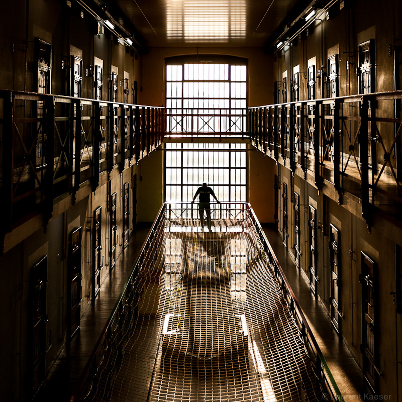 Image assez sombre, en contre-jour. Un personnage se tient pencheé et regarde vers le bas où est tendu un grand filet qui protège le fond de la cour.