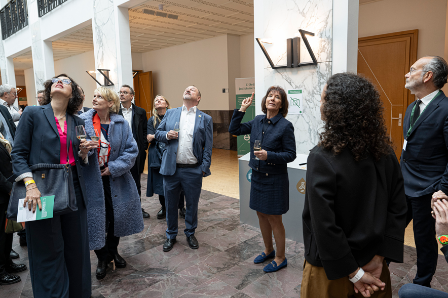 Les invités sont sous la verrière du bâtiment. Madame Bernel pointe son doigt ver le haut, tout le monde a la tête tournée vers la verrière.