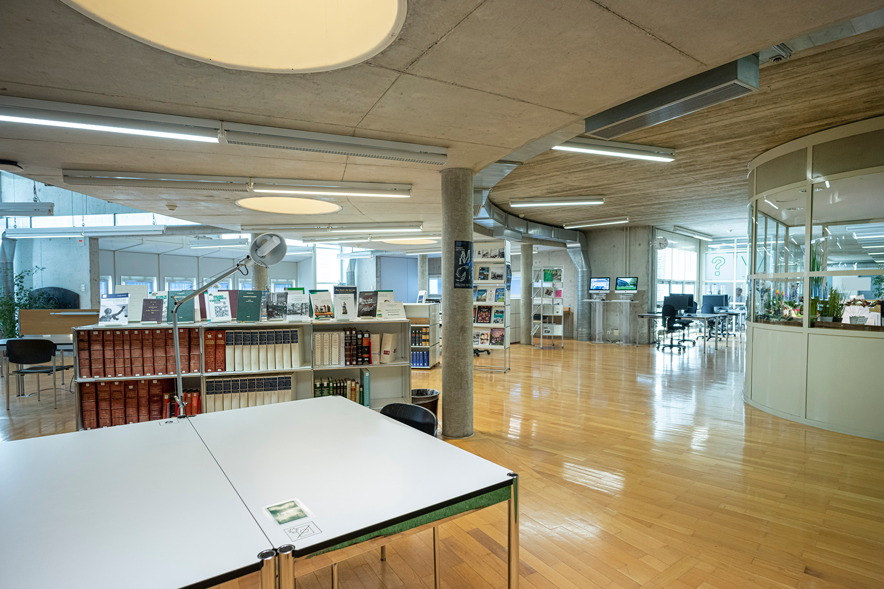 La salle de forme arrondie. Table, bibliothèque, écrans d'ordinateur et fenêtres.