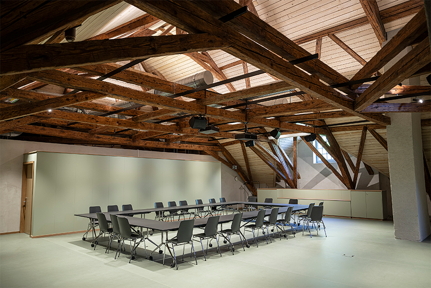 une grande salle où l'on voit la poutraison de la toiture. Une grande table de conférence avec ses chaises.