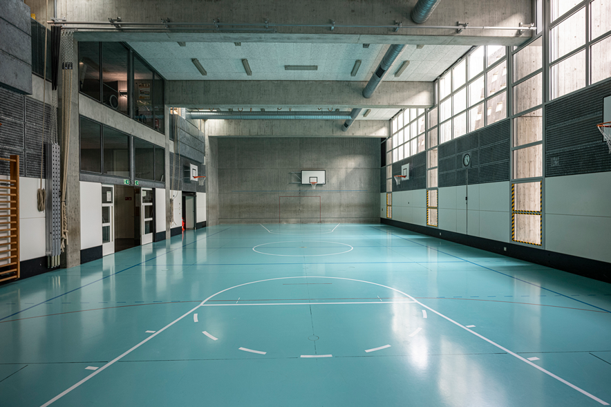 vue de la salle de gym, son sol avec les marques pour le basket ou le hand-ball, son haut plafond et ses murs en béton.