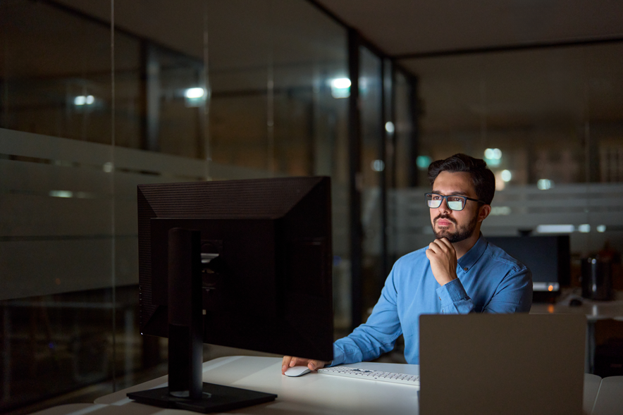 Un homme derrière son écran dans un bureau sombre.
