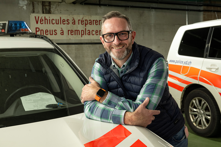 Steve Cruchon, qui a une quarantaine d'années, est appuyé sur le capot d'une voiture de police. Un autre véhicule, type fourgon, est visible derrière. On est dans un garage souterrain. Au mur, un panneau : "Véhicules à réparer. Pneus à remplacer".