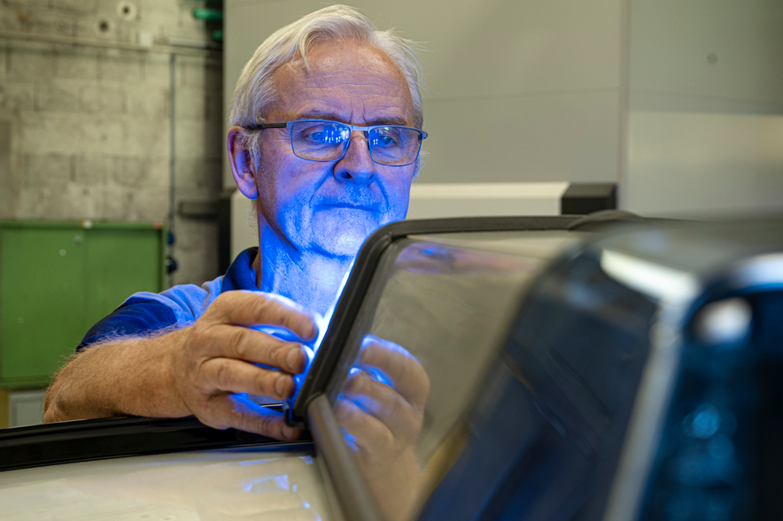 Un mécanicien règle le feu bleu sur le toit d'une voiture. La lumière se reflète sur son visage et ses lunettes.