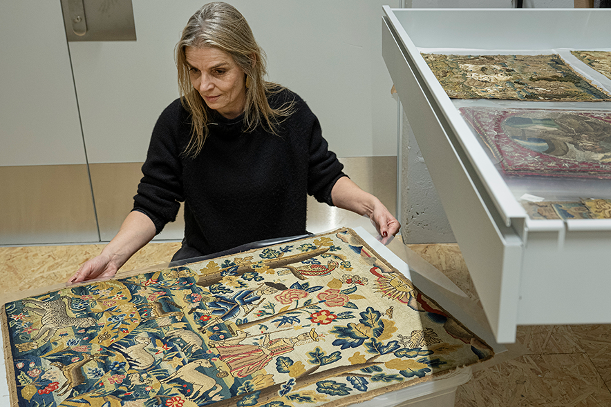 Madame Junet tient entre ses mains la tapisserie montrant la scène pastorale en question.